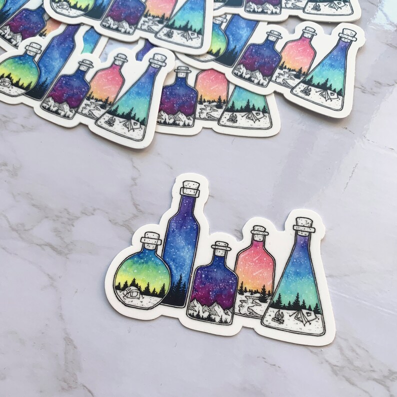 May include: Five glass bottles with cork stoppers, each containing a different watercolor scene of a starry night sky, mountains, and a forest. The bottles are arranged in a row on a white background.