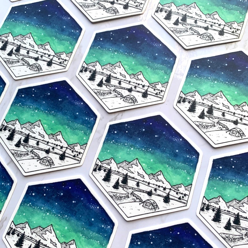May include: A set of hexagonal stickers featuring a watercolor illustration of a mountain range under a starry sky with a green aurora borealis. The mountains are outlined in black and a small tent is visible in the foreground.