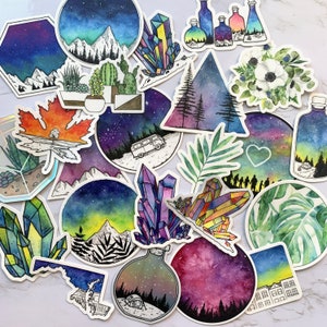 K&ouml;nnte beinhalten: Eine Sammlung bunter Aufkleber mit verschiedenen Designs, darunter Kristalle, Berge, Blumen und ein Van. Die Aufkleber sind im Aquarell-Stil mit einem sternenklaren Nachthimmel als Hintergrund gemalt.