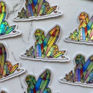 Könnte beinhalten: Ein Set mit bunten, schillernden Kristall-Stickern. Jeder Sticker zeigt einen Cluster von Kristallen in verschiedenen Blautönen, Grüntönen, Gelbtönen, Orangetönen und Rottönen. Die Kristalle sind in einem verspielten Stil mit glänzendem Finish gezeichnet.