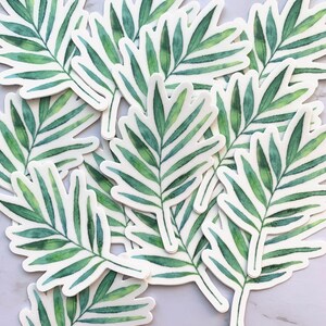 May include: A collection of green and white palm leaf stickers. The stickers are cut out in the shape of a palm leaf and have a watercolour effect.
