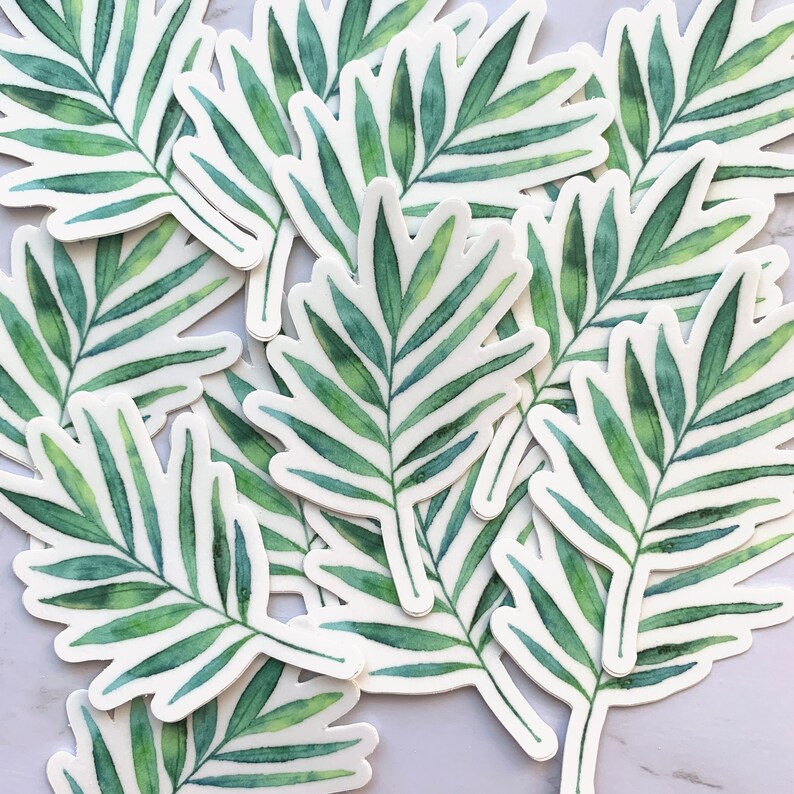 May include: A collection of green and white palm leaf stickers. The stickers are cut out in the shape of a palm leaf and have a watercolour effect.