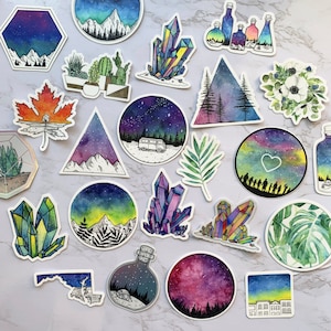 May include: A collection of 18 watercolor stickers featuring various designs, including crystals, mountains, stars, and plants. The stickers are all on a white background.