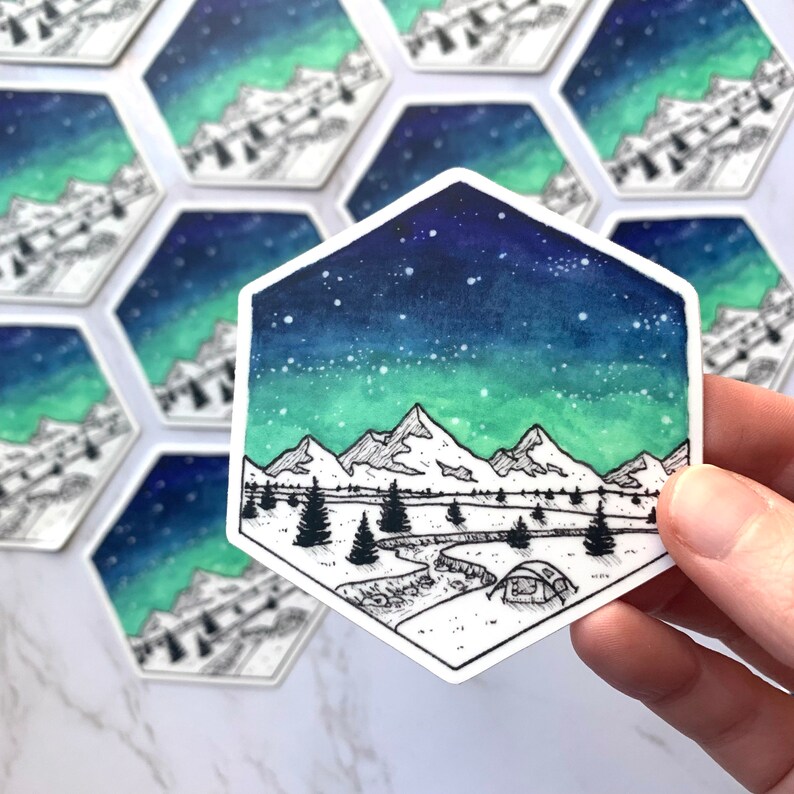 May include: A hexagonal sticker with a watercolor illustration of a mountain range under a starry sky with a green and blue aurora borealis. The mountains are outlined in black and there is a small tent in the foreground.