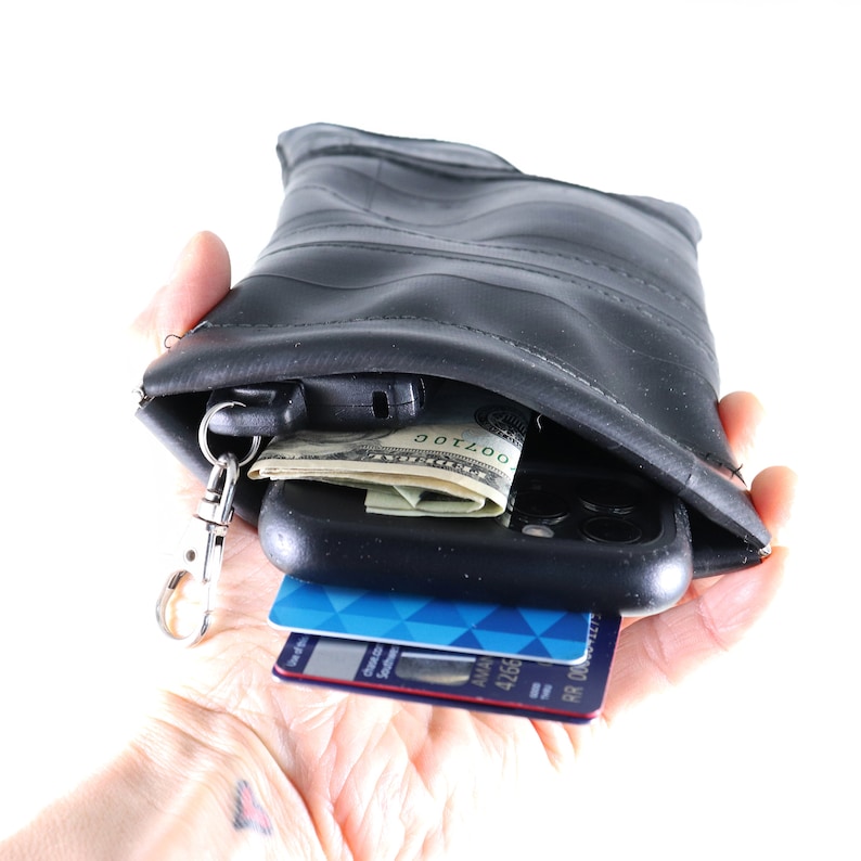 May include: A black recycled inner tube wallet with a zipper closure. The wallet is open and contains a smartphone, credit cards, cash, and a key chain.