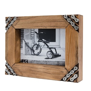 May include: A wooden picture frame with a black and white photo of a child's tricycle. The frame is decorated with silver bicycle chain links in the corners.