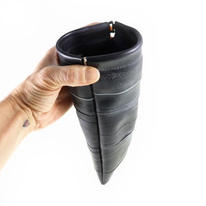 May include: A black zippered pouch made from recycled inner tubes. The pouch is folded in half and held in a hand.