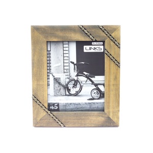 May include: A brown wooden picture frame with a black and white photo of a child's tricycle. The frame has a decorative chain design around the edges. The frame is labeled "8 x 10 frame" and "LINKS".
