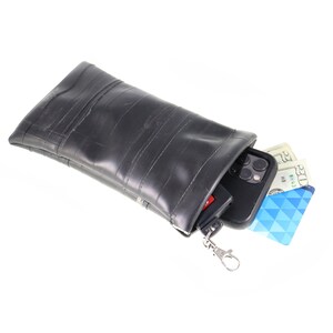 May include: A black recycled inner tube phone case with a zipper closure and a silver keychain. The case is open and a black smartphone, a credit card, and cash are inside.