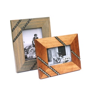 May include: Two wooden picture frames, one gray and one brown, each with a bicycle chain accent on the corners. The frames hold black and white photos of cyclists and a bicycle. The frames are rectangular.