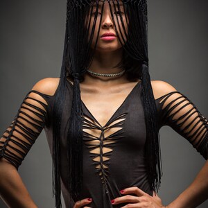 Puede incluir: Una mujer con un top negro con un dise&ntilde;o de corte y un sombrero negro con flecos. El sombrero le cubre la cara.