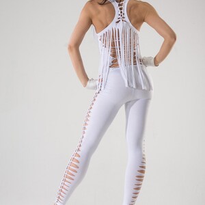 Puede incluir: Un conjunto blanco con una parte superior de flecos y leggings con recortes. La parte superior tiene un dise&ntilde;o de cruz en la espalda. La modelo lleva una gorra de b&eacute;isbol negra.