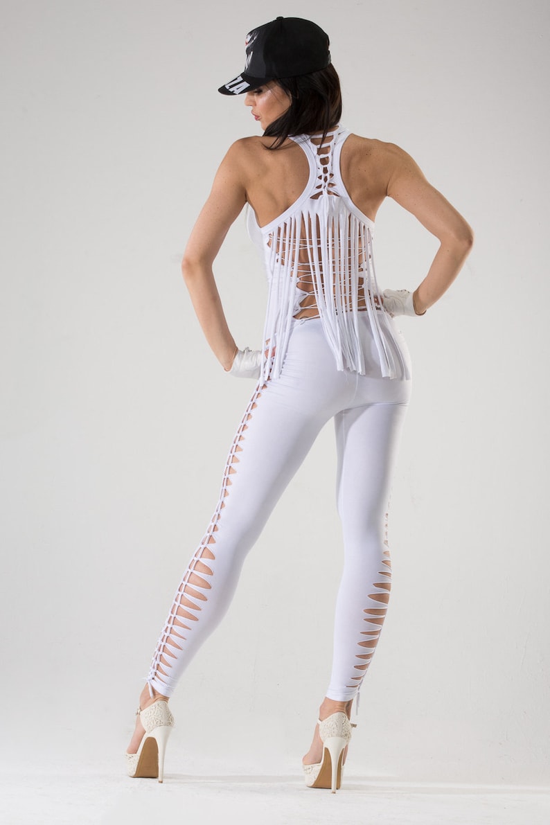 Puede incluir: Un conjunto blanco con una parte superior de flecos y leggings con recortes. La parte superior tiene un dise&ntilde;o de cruz en la espalda. La modelo lleva una gorra de b&eacute;isbol negra.