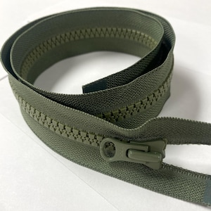 May include: A coiled olive green plastic zipper featuring large molded teeth and a matching olive green pull tab. The zipper tape is made of a woven fabric, and the slider is positioned near the end of the coil, showing a functional design.