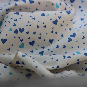 May include: A white fabric with a blue and green heart pattern. The fabric is folded and draped.