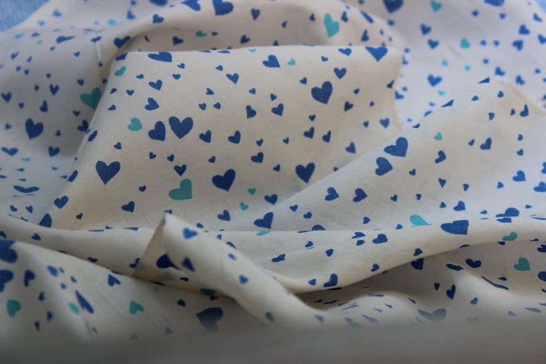 May include: A white fabric with a blue and green heart pattern. The fabric is folded and draped.