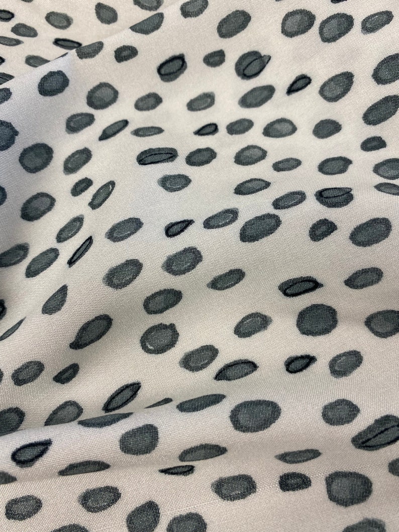 May include: White fabric with a black polka dot pattern. The fabric is textured and has a subtle sheen.