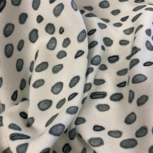 May include: White fabric with a grey and black abstract pattern of small, irregular shapes. The fabric is folded and textured.
