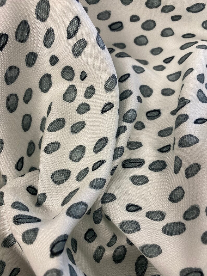 May include: White fabric with a grey and black abstract pattern of small, irregular shapes. The fabric is folded and textured.