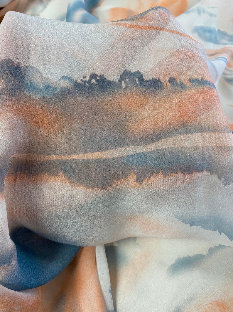 Puede incluir: Primer plano de una tela fluida con un dise&ntilde;o de acuarela. La tela presenta una escena de paisaje con tonos de azul, naranja y gris. El dise&ntilde;o se asemeja a una puesta de sol sobre una masa de agua.