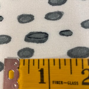 May include: A close-up of a yellow measuring tape with black markings. The tape reads "1" and "2" and has the words "Fibre-Glass" printed on it. The tape is lying on a white fabric with a black and white polka dot pattern.