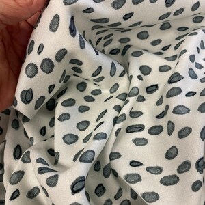 May include: White fabric with a scattered pattern of dark grey spots. The fabric is wrinkled and folded.