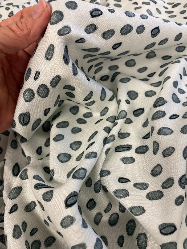 May include: White fabric with a scattered pattern of dark grey spots. The fabric is wrinkled and folded.