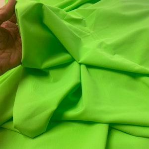 Puede incluir: Tela verde neón brillante con una textura suave y sedosa. La tela está doblada y drapeada, mostrando su flexibilidad.