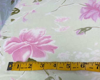 May include: A close-up of a yellow measuring tape with black markings. The tape reads "Fiber-Glass" and "Made in China". The tape is lying on a light green fabric with a pink floral pattern.