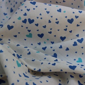 May include: White fabric with a blue and turquoise heart pattern. The fabric is folded and draped.