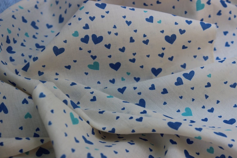 May include: White fabric with a blue and turquoise heart pattern. The fabric is folded and draped.