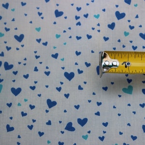 May include: White fabric with a blue and teal heart pattern. A yellow measuring tape with the numbers "1", "2", and "3" is visible.