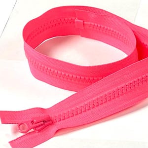 May include: A bright neon pink plastic zipper featuring a matching pink slider and pull tab. The zipper tape is made of a woven fabric, and the teeth are molded plastic, arranged in a continuous coil that is looped into a circular shape.