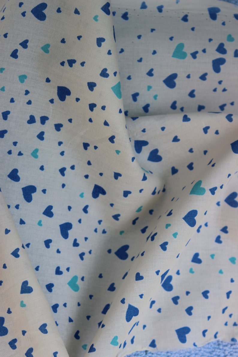 May include: White fabric with a blue and light blue heart pattern. The fabric is folded in half and the pattern is visible on both sides.