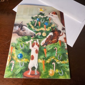 May include: A Christmas card featuring a green Christmas tree decorated with candy canes, ornaments, and carrots. Two horses and two dogs are decorating the tree. The dogs are wearing red collars and the horses have brown and white markings.