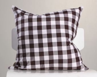 May include: A brown and white checkered pillow rests on a white chair. The pillow has a classic gingham pattern, with alternating squares of brown and white. The pillow is soft and plush, perfect for home decor.