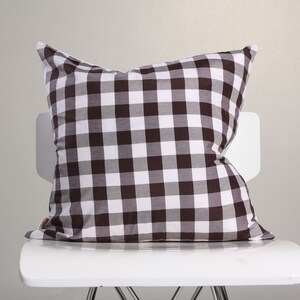 May include: A brown and white checkered pillow rests on a white chair. The pillow has a classic gingham pattern, with alternating squares of brown and white. The pillow is soft and plush, perfect for home decor.