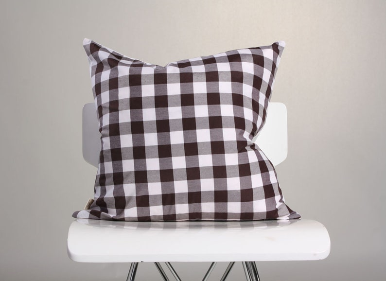 May include: A brown and white checkered pillow rests on a white chair. The pillow has a classic gingham pattern, with alternating squares of brown and white. The pillow is soft and plush, perfect for home decor.