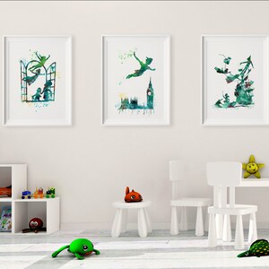 May include: Three watercolor prints featuring Peter Pan flying with a green and blue color scheme. The prints are framed in white and hung on a white wall.
