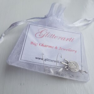 Earringts are shown in packaging.  The earrings are attached to a small card with Glitterartis details on it.  The card and earrings are in a white organza bag.