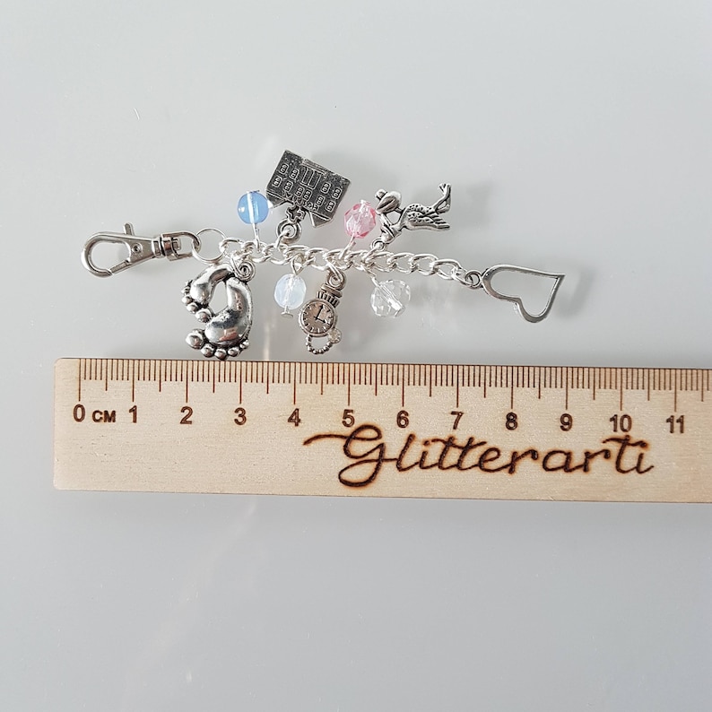 May include: Silver charm bracelet featuring a selection of charms, including a house, a clock, a heart, and a pair of baby footprints. The bracelet measures approximately 10 cm in length and has a silver clasp.