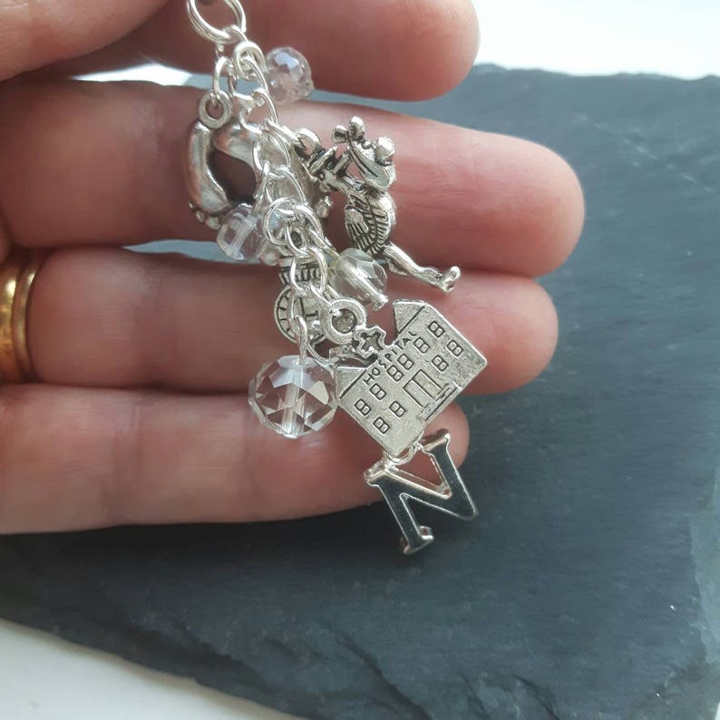May include: Silver charm bracelet featuring a selection of charms, including a house, a clock, a crystal, and the letter N.