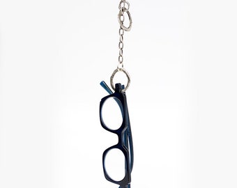 May include: A silver chain with two silver rings hangs from the ceiling. A pair of black reading glasses with blue arms are attached to the chain.