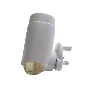 May include: A white electric plug-in air freshener with a gold-coloured diffuser. The air freshener is designed to be plugged into a standard electrical outlet.