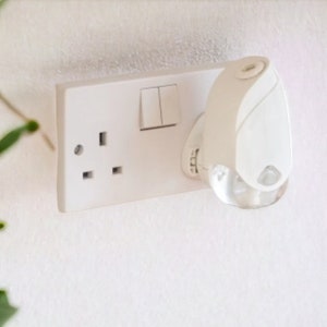 May include: A white electrical socket with a white plug-in nightlight. The nightlight has a clear plastic lens and a small sensor on the front.