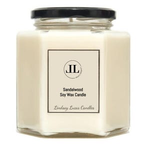 May include: A square, clear glass jar candle with a black lid. The candle has a cream-colored wax and a label that reads "Sandalwood Soy Wax Candle" and "Lindsay Lucas Candles". The jar has a hexagonal shape.