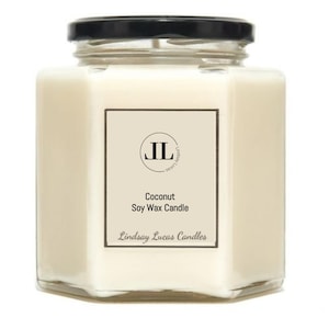 Puede incluir: Una vela en tarro de vidrio transparente de forma cuadrada, con tapa negra. La vela tiene un interior de cera blanca y una etiqueta rectangular con el texto "Coconut Soy Wax Candle" y el nombre de la marca.