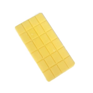 Puede incluir: Una barra rectangular de cera amarilla, dividida en 24 cuadrados, sobre un fondo blanco. La barra de cera está en ángulo, mostrando su diseño segmentado. El color es un amarillo pálido y cremoso.