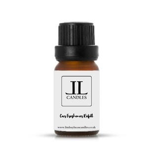 May include: A small brown glass bottle with a black cap. The bottle has a white label with the text "JL Candles" and "Car Freshener Refill" and the website address "www.lindsaylucascandles.co.uk".