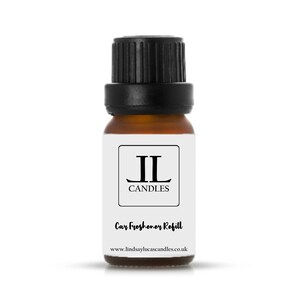 May include: A small brown glass bottle with a black lid. The bottle is labelled with the text "JL Candles" and "Car Freshener Refill". The website address "www.lindsaylucascandles.co.uk" is printed on the label.